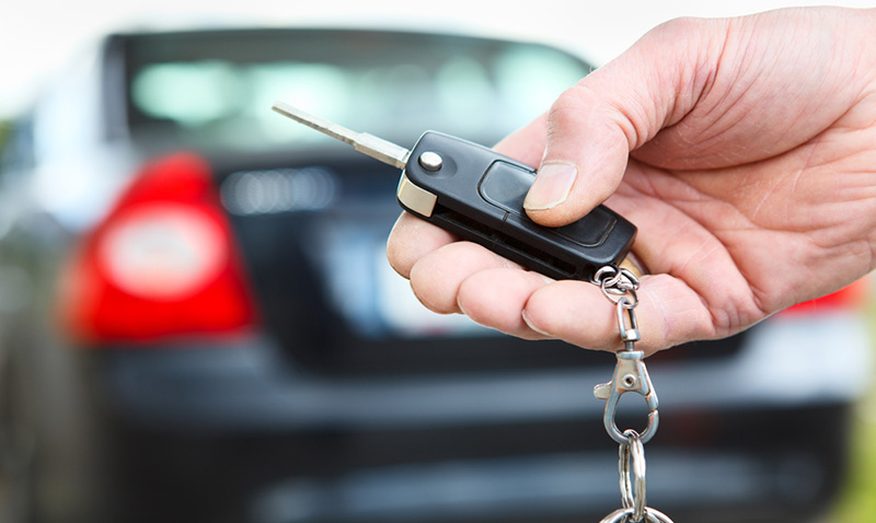Hand holding a flip key fob next to a car